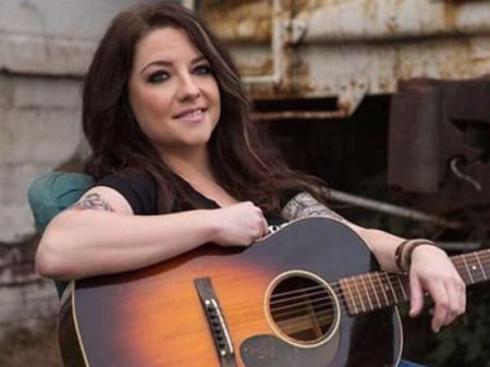 Ashley McBryde poses a picture with a guitar in her hand.